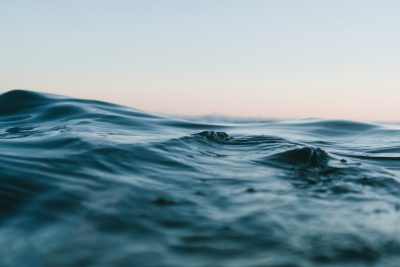 Photograph of a close-up shot of calm ocean water at dusk in muted colors from a low angle view with a shallow depth of field, beautiful. --ar 128:85