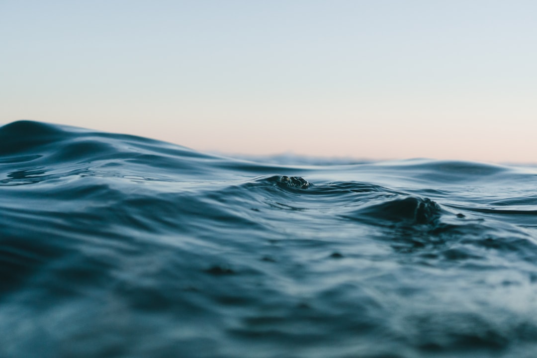 Photograph of a close-up shot of calm ocean water at dusk in muted colors from a low angle view with a shallow depth of field, beautiful. –ar 128:85