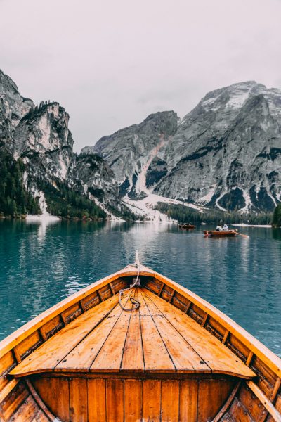 View from the bow of a wooden boat on Lake Braies in Dolomites, Italy, with snowcapped mountains in the background, in the style of unsplash photography. --ar 85:128