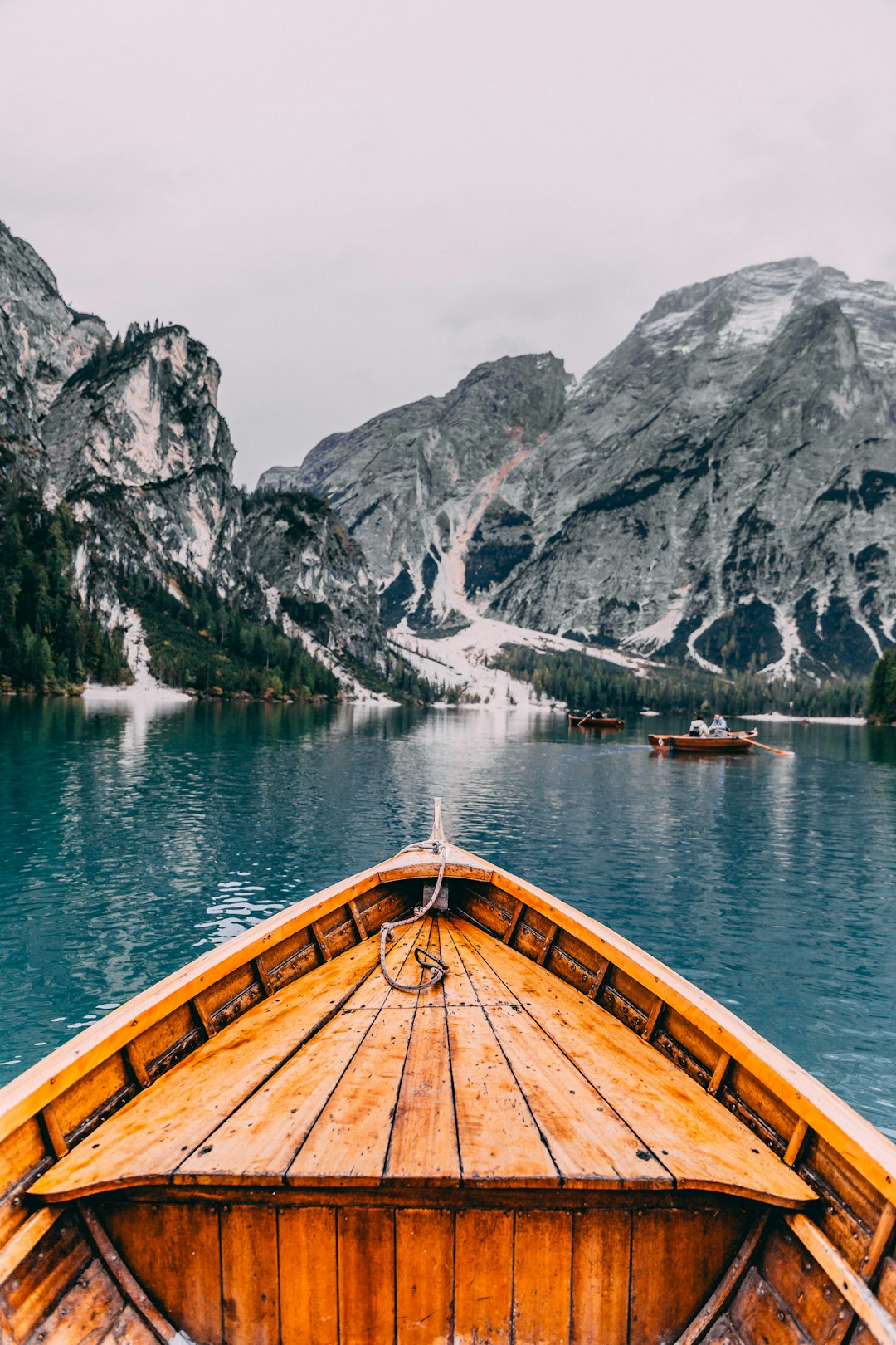 View from the bow of a wooden boat on Lake Braies in Dolomites, Italy, with snowcapped mountains in the background, in the style of unsplash photography. –ar 85:128