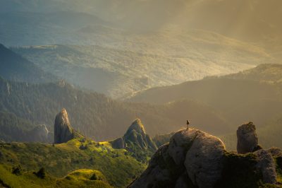 photography of the Carpathian Mountains, a person standing on top of rocks with green grass and forest in the background, golden hour lighting, epic landscape, wide shot, unsplash photography in the style of unsplash, --ar 128:85