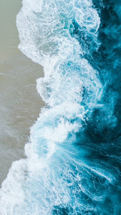 Beautiful aerial view of the waves crashing on the beach, perfect for a mobile phone background wallpaper. Aerial photography with blue and white tones of sea waves splashing on the surface and sand texture with high definition details, high resolution, high quality, high sharpness and high focus in a professional photograph. --ar 71:128