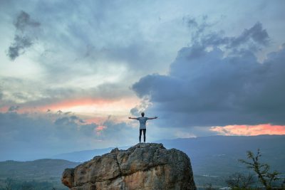 A man standing on top of the mountain with his arms spread out, feeling free and happy, with beautiful clouds in front of him at sunset, a magnificent view behind him, symbolizing freedom and success, with a wide angle camera shot. The photo was taken using a Canon EOS R5 and Fujifilm Provia film, highlighting the contrast between the light blue sky and dark grey rocks. in the style of [Ansel Adams](https://goo.gl/search?artist%20Ansel%20Adams). --ar 128:85