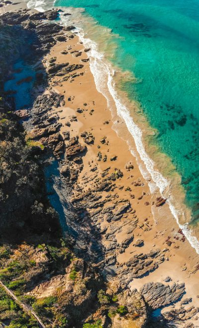 Beautiful beach aerial view in Australian coast, clear turquoise water, golden sand and rocks, sunlight, high resolution photography, high definition, sharp focus, depth of field, natural light, natural colors, professional color grading, high quality --ar 77:128