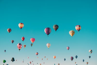 A vibrant array of hot air balloons floating gracefully in the clear blue sky, creating an enchanting and whimsical scene that is sure to make you feel happy. Wide shot, full body, in the style of canon eos r5. --ar 128:85