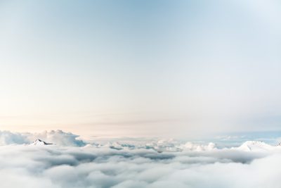 A serene sky above the clouds, with distant snowcapped mountains visible through fluffy white fog, creating an ethereal and dreamy atmosphere. The sky is clear and blue, adding to its peacefulness. A small plane can be seen flying in the distance against the backdrop of soft pastel colors. This scene evokes tranquility and serenity, perfect for creative projects that evoke calm emotions or convey peaceful vibes. --ar 128:85