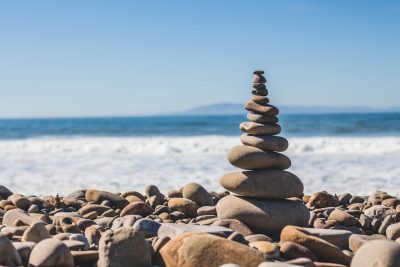 Photo of balanced stones tower on the beach, blue sky and ocean background, in the style of Canon R5. --ar 128:85