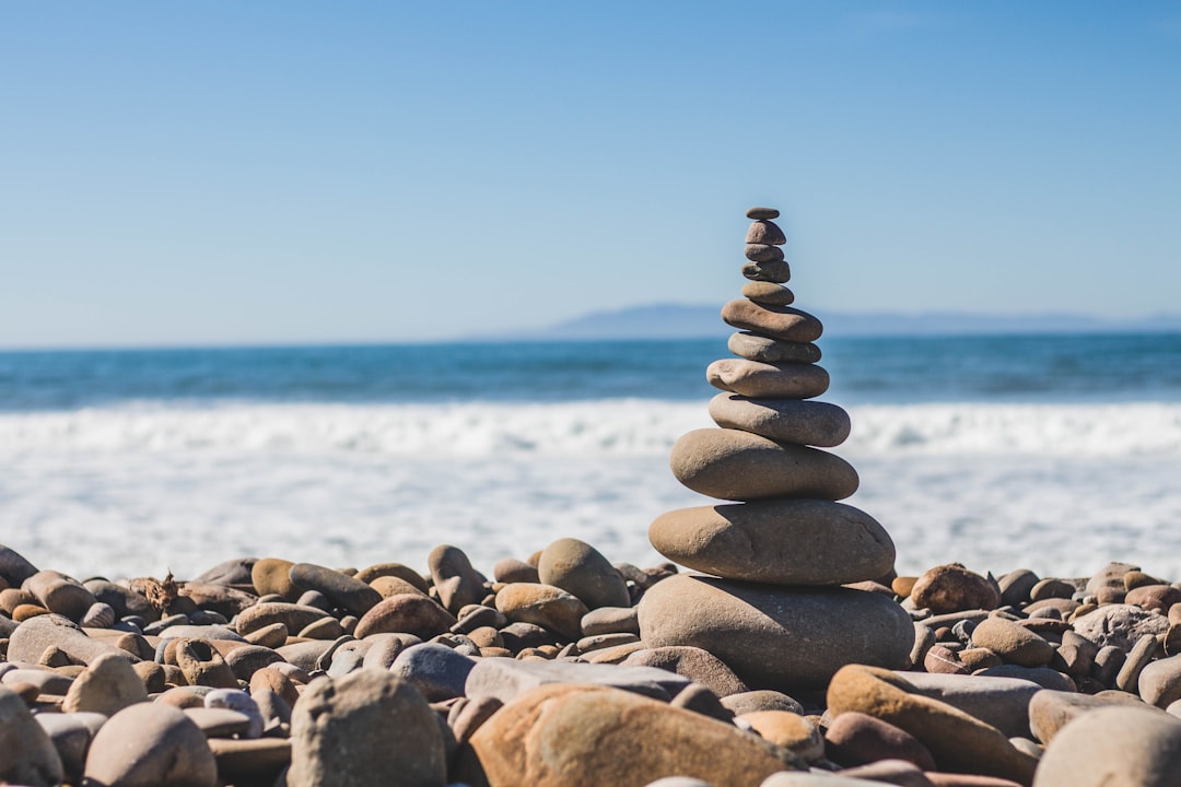 Photo of balanced stones tower on the beach, blue sky and ocean background, in the style of Canon R5. –ar 128:85