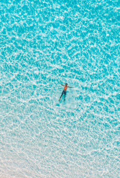 aerial view of surfer in the turquoise ocean, crystal clear water, minimalist photography, white sand beach. --ar 43:64