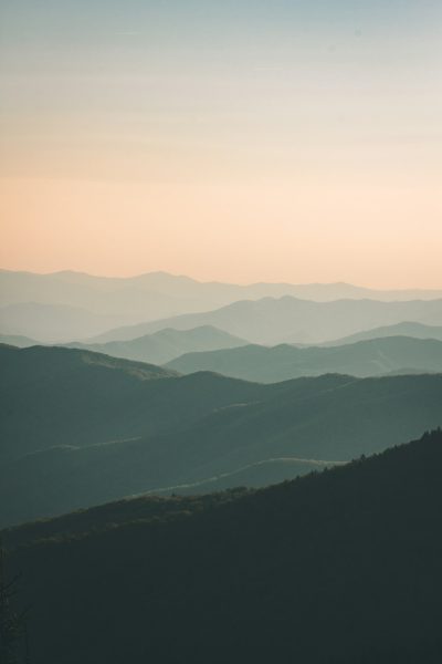 minimalistic, vast mountainscape with subtle color gradients and soft lighting in muted tones create a serene atmosphere. The view from the top of Great Smoky Mountains National Park at sunrise shows a silhouette of the blue ridge mountain in the background with no clouds or sky. A peaceful and tranquil mood comes from the wide angle shot and simple yet elegant composition that focuses on the natural beauty and serenity. --ar 85:128