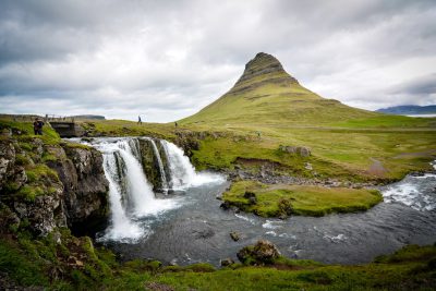 Photo of a waterfall in Iceland with the famous mountain in the background, it is purely white and green, there are some people walking around it, landscape photography, cloudy sky, photography from unsplash, wide angle lens --ar 128:85