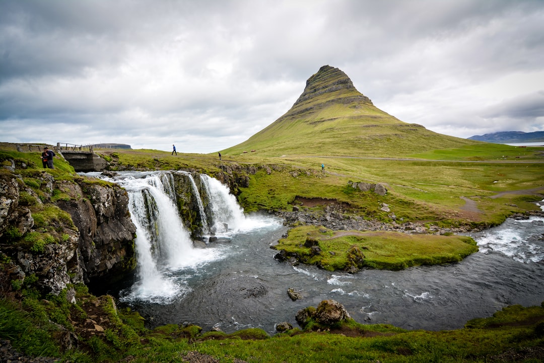 Photo of a waterfall in Iceland with the famous mountain in the background, it is purely white and green, there are some people walking around it, landscape photography, cloudy sky, photography from unsplash, wide angle lens –ar 128:85
