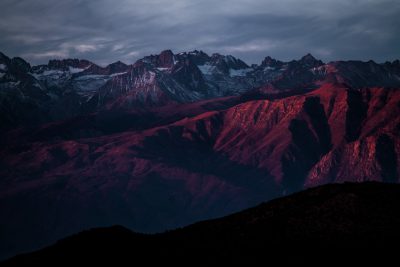 A dramatic photo of the mountains in Dagestan, at night, with pink and red tones, creating a shadow play, against a dark sky, with mountains in the background, with high contrast, and sharp details, shot on a Sony Alpha A7 III camera with a Zeiss Batis lens, in the style of no particular artist. --ar 128:85