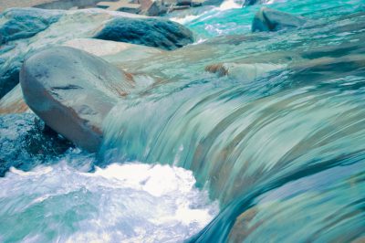 A close up of water flowing over rocks, blue and teal watercolor in the style of smooth glassy river with light aquamarine waves, hyper realistic photography in the style of national geographic photo, high definition --ar 128:85