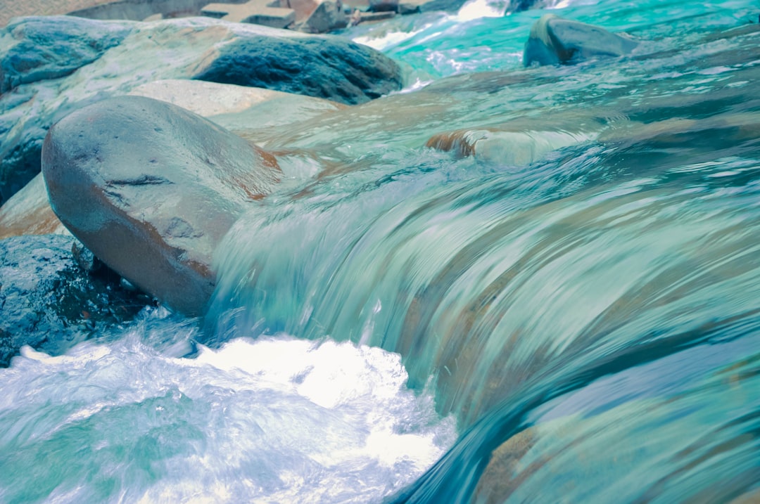 A close up of water flowing over rocks, blue and teal watercolor in the style of smooth glassy river with light aquamarine waves, hyper realistic photography in the style of national geographic photo, high definition –ar 128:85