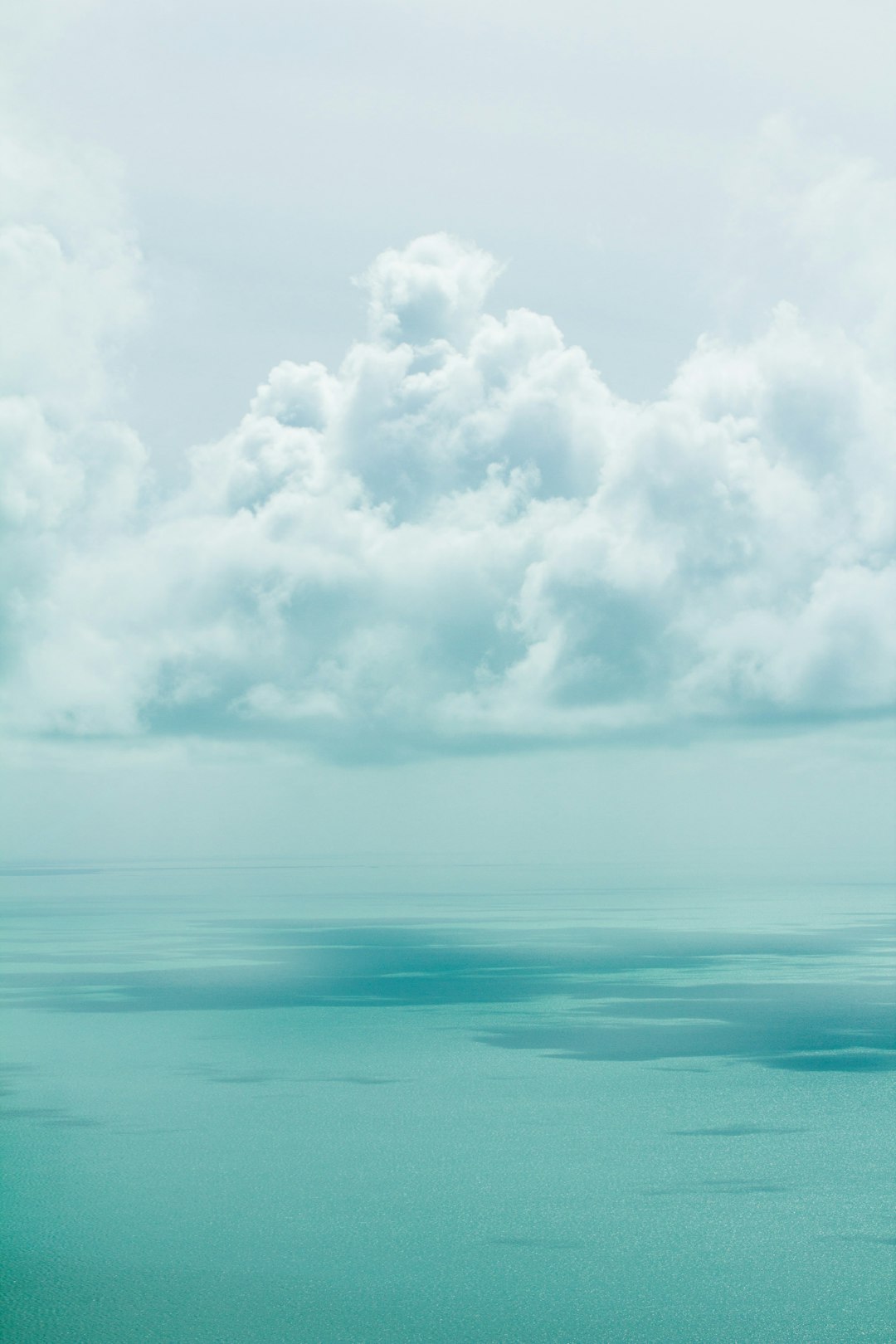 minimalist photo of the sea and clouds on the horizon, sky with teal color tones creating a calming effect. –ar 85:128