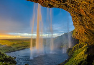 Icelandic waterfall from inside the cave, sunset, golden light, blue sky, green grassy valley, water in motion, long exposure, photo realistic, in the style of national geographic photography --ar 16:11