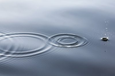 A photo of small ripples in the water, with one drop creating circular waves on the calm grey surface. The focus is sharp and clear, capturing the intricate details of each ripple's shape and size. This scene evokes tranquility and harmony as these gentle splashes create delicate patterns across the still waters in the style of calm waters. --ar 128:85