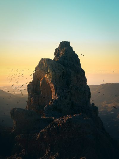 a photo of the top of mountain in morocco, a huge rock with birds flying around it, sunset light, cinematic, high resolution photography --ar 3:4