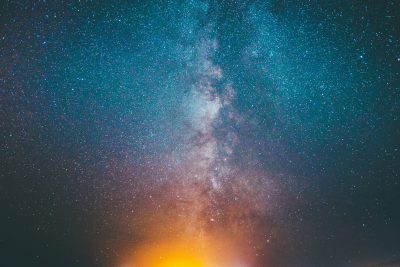 Starry sky, Milky Way, starry background, night sky, bright stars, star field, sky full of twinkling stars, distant light on the horizon, starry cloud in the center of frame, blue and yellow color scheme, orange glowing fire pit at bottom right corner, space photography, captured by Sony Alpha A7 III camera with Sony FE2485mm f/3.6 lens --ar 128:85