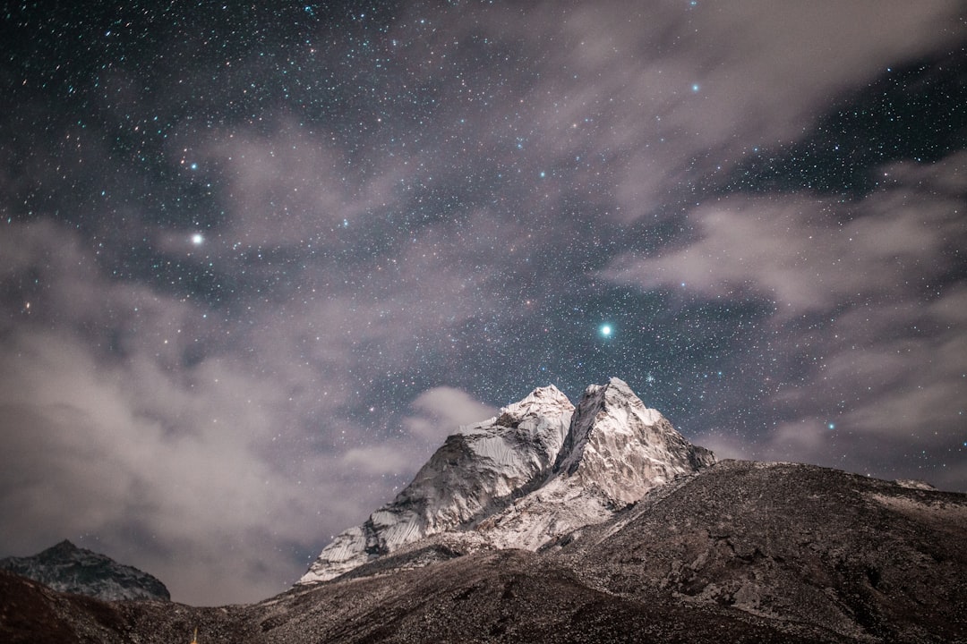 Starry night sky over the Himalayas, Ama Dabron mountain peak in earthen colors of white and gray with snow on top, clouds in the background, in the style of Nikon Z7 II, f/2 lens, starry composition. –ar 128:85