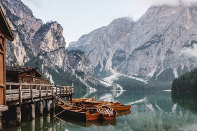 Photo of Braies lake with rowing boats and wooden buildings, Dolomites in background, cinematic light, in the style of unsplash photography. --ar 128:85