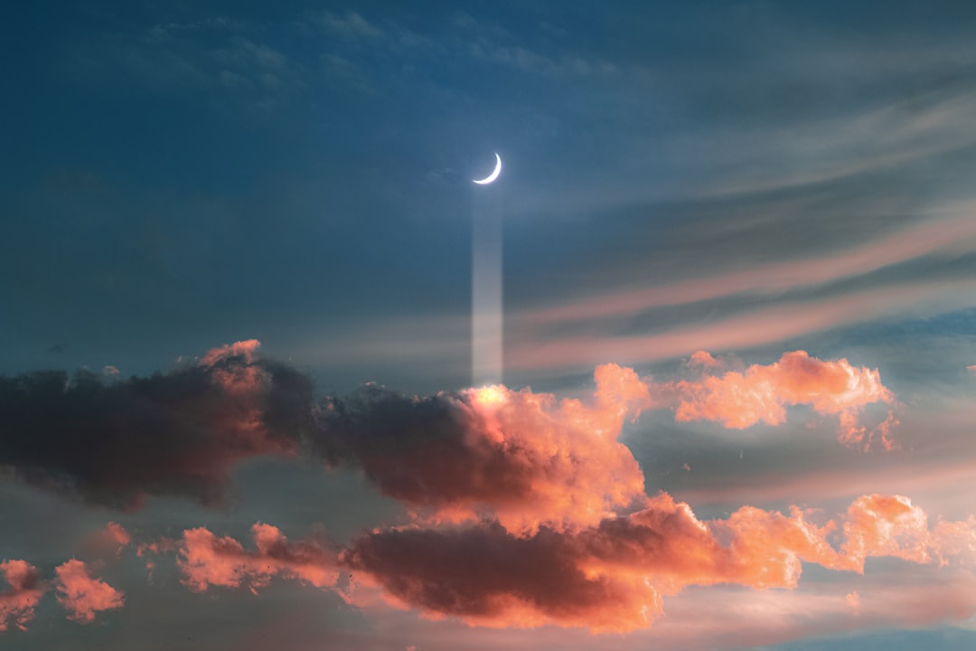 The crescent moon is shining in the sky, with pink clouds and a blue sky. A beam of light shines on it from behind the cloud, creating an ethereal scene with dreamy colors and a cinematic composition in the style of fantasy and surrealism. The photography has a high resolution. –ar 128:85