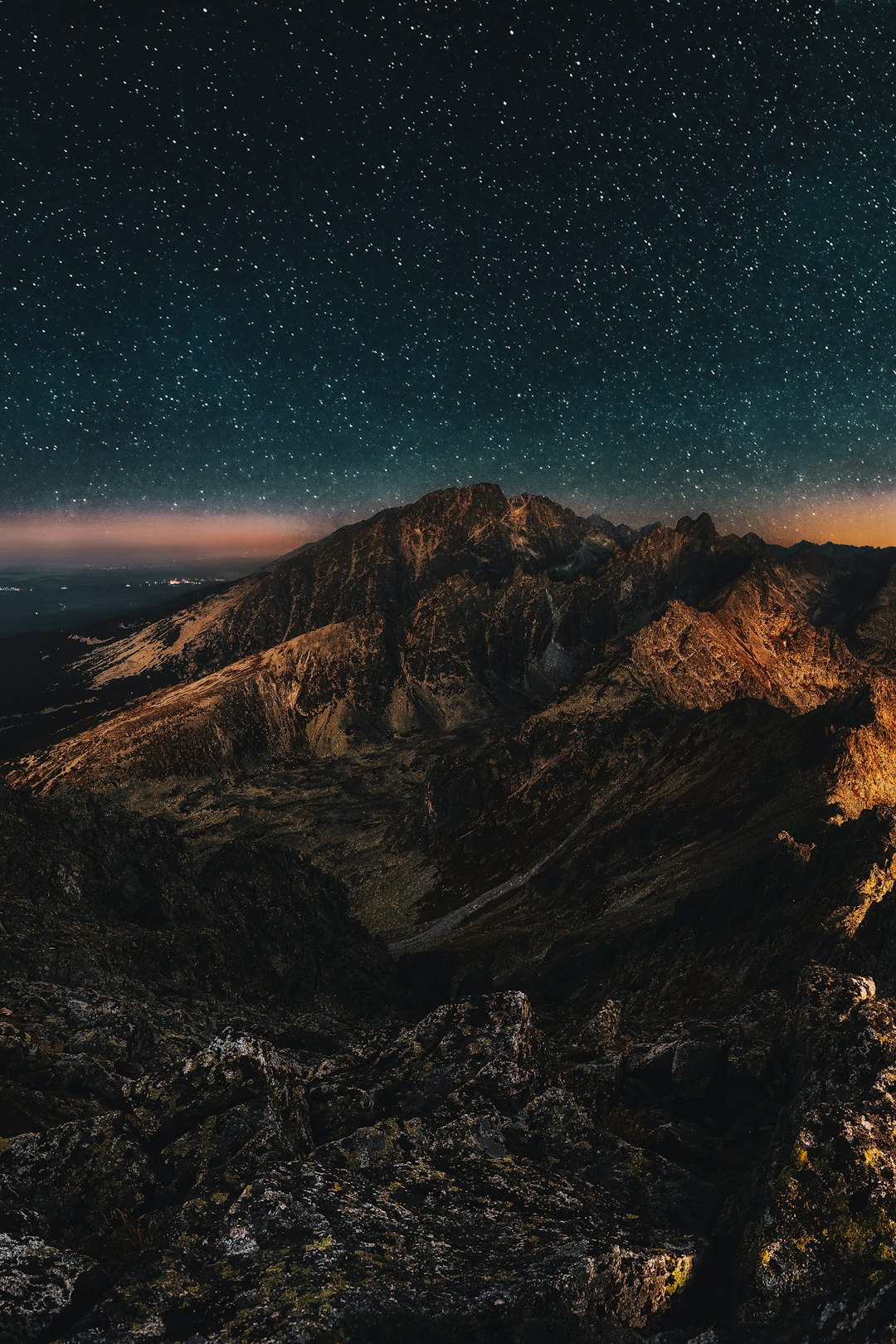 Cinematic photo of the Tatra Mountains at night, with stars in the sky and a glow from an iPhone on top of one mountain. The scene is illuminated by moonlight, creating deep shadows between rocks and mountains, with subtle light effects adding depth to the composition. In closeup view, the rugged landscape appears mystical under starry skies in the style of moonlight. –ar 85:128