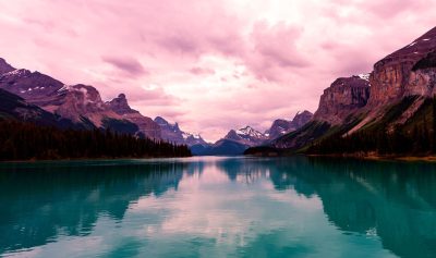 A serene turquoise lake surrounded by mountains under a pink sky, capturing the tranquil beauty of nature in a Canadian national park. The calm waters reflect the majestic peaks and fluffy clouds, creating an enchanting scene that evokes peace and harmony with natural landscapes in the style of a Chinese painter. --ar 128:75