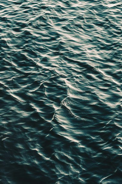 A close up of water ripples on the surface of an ocean, dark and moody with a monochromatic color scheme and grainy film filter in the style of vintage photography, from a top down view. --ar 85:128