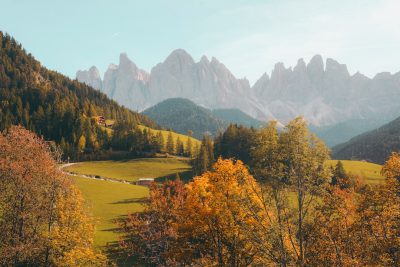 cinematic photo of the Dolomites in Italy, green and yellow trees with mountains behind, autumn colors, clear sky, bright colors, sunny day, cinematic --ar 128:85