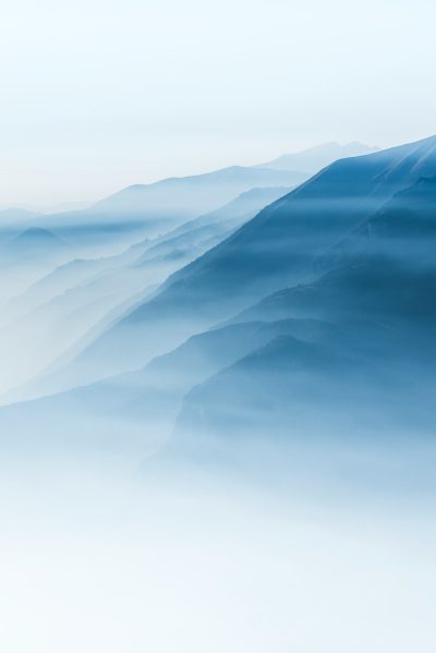 Minimalist mountain landscape with layers of fog, ethereal blue hues, white background, tranquil and dreamy atmosphere, mist-covered peaks, high-resolution photographic style, soft focus on the edges for a depth effect. --ar 85:128