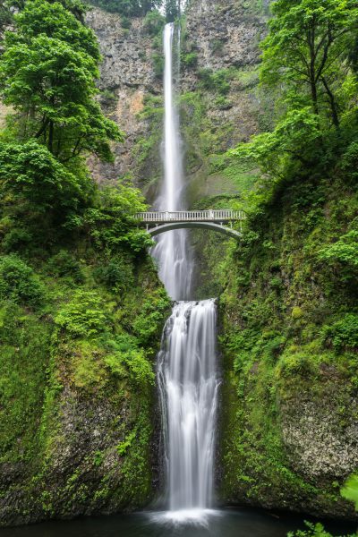 Multor Waterfall in Oregon, USA with a bridge over the waterfall, lush greenery and vibrant colors of springtime nature, perfect for a travel poster style, high resolution, high quality, hyper realistic, sharp focus, depth of field, landscape photography, professional camera shot, natural lighting, beautiful, detailed, intricate details, masterpiece, best resolution, high definition, no grainy texture, no noise in the style of a professional photographer. --ar 85:128