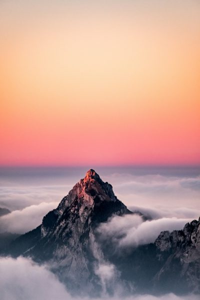 A photo of the top peak of Kitzbuhel in Austria with pink and orange sky, taken from above, foggy clouds below, shot on Sony Alpha A7 III --ar 85:128