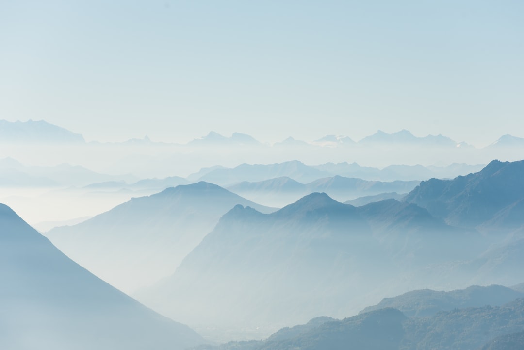 The light blue sky is surrounded by the misty mountains, creating an ethereal and dreamlike atmosphere. The distant peaks blend into each other in soft shades of gray against the backdrop of a clear sky. Aerial photography techniques capture the vastness of these mountainous landscapes, adding depth to the scene. This photo was taken with Canon EOS R5 using a wideangle lens at f/4 aperture setting, capturing every detail of the majestic landscape. –ar 128:85