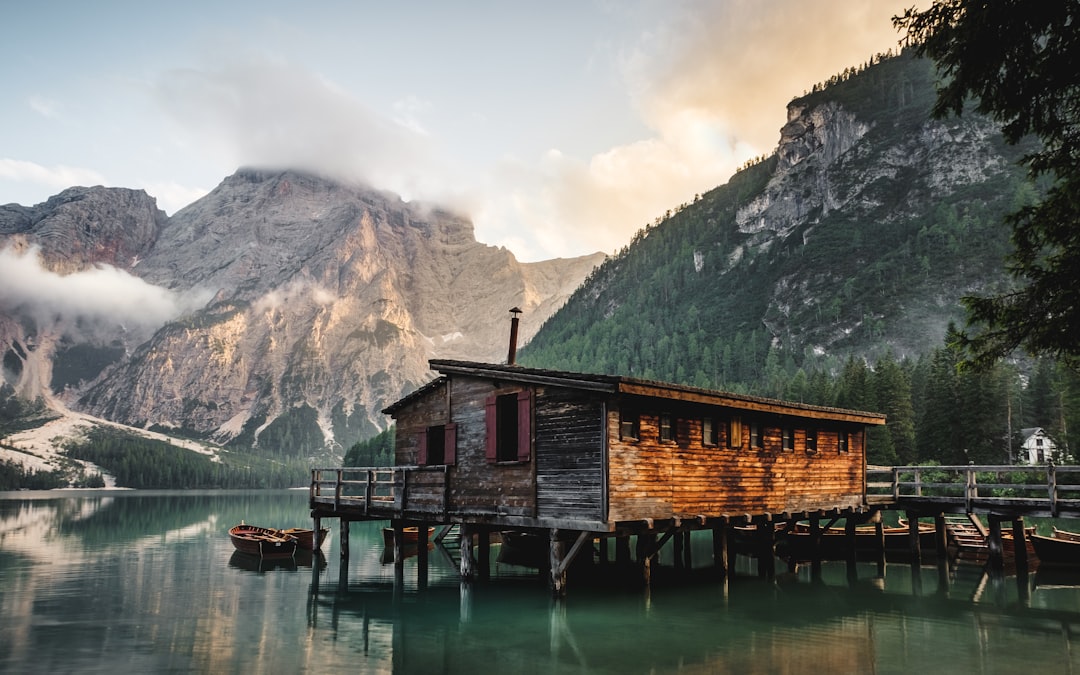 wooden cabin on the lake braies in dolomites in the style of seneryrutIREXqueladornbdüsseldorf blending natural colors and the beautiful mountains of south italy, with the green forest, wooden dock and boat at sunrise, stock photo, unsplash photography –ar 8:5