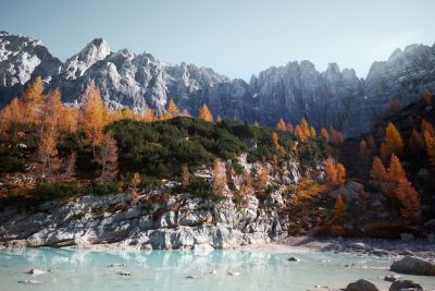 Cinematic shot of mountains with larch trees and a lake in the valley, alpine nature photography, turquoise water, autumn season, cinematic shot, realistic, high resolution, hyper detailed, in the style of Unreal Engine. --ar 128:85