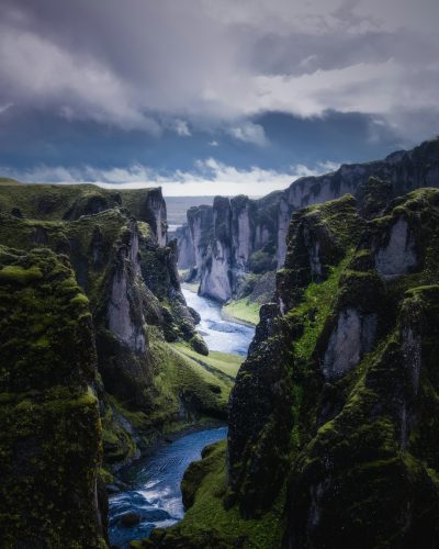 landscape photography of Fjadafr Though in Iceland, with green mossy cliffs and dark blue river flowing through the canyon, dramatic sky, canon eos r5 --ar 51:64