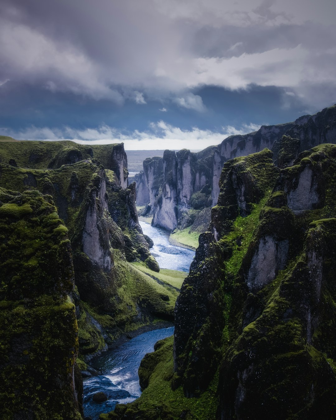 landscape photography of Fjadafr Though in Iceland, with green mossy cliffs and dark blue river flowing through the canyon, dramatic sky, canon eos r5 –ar 51:64