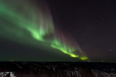 Beautiful view of the northern lights in the wilderness, with snow-covered hills and greenish purple colors dancing across the night sky. The photo was taken from atop with the Nikon D850 camera using an f/2 lens at ISO speed 36k, capturing the mesmerizing beauty of nature's symphony. --ar 128:85