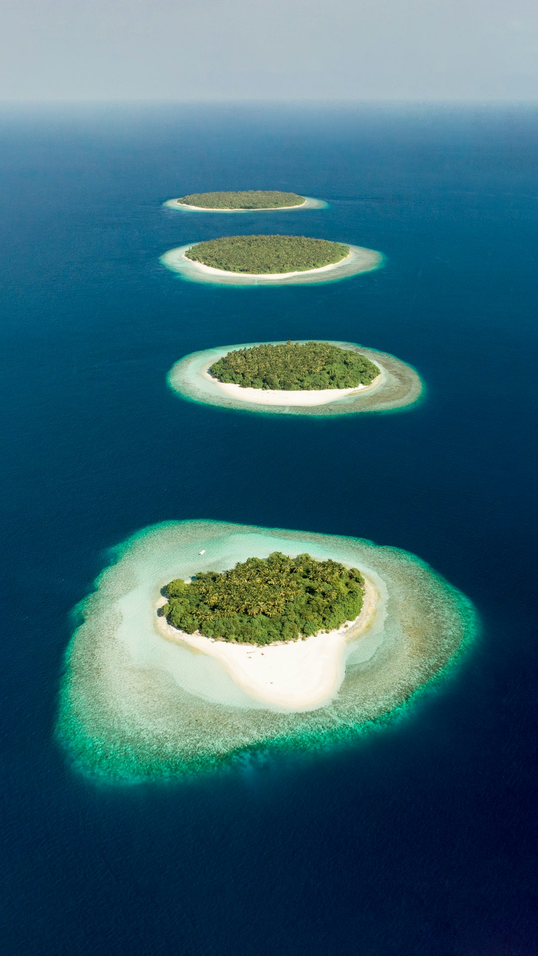 Aerial view of the group islands in Maldives, with lush greenery and pristine white sandy beaches. The turquoise waters create beautiful lagoons that reflect sunlight, creating a stunning scene from above. High resolution photography. This is an award winning photograph by National Geographic magazine. Shot on Canon K35 Prime lenses –ar 9:16