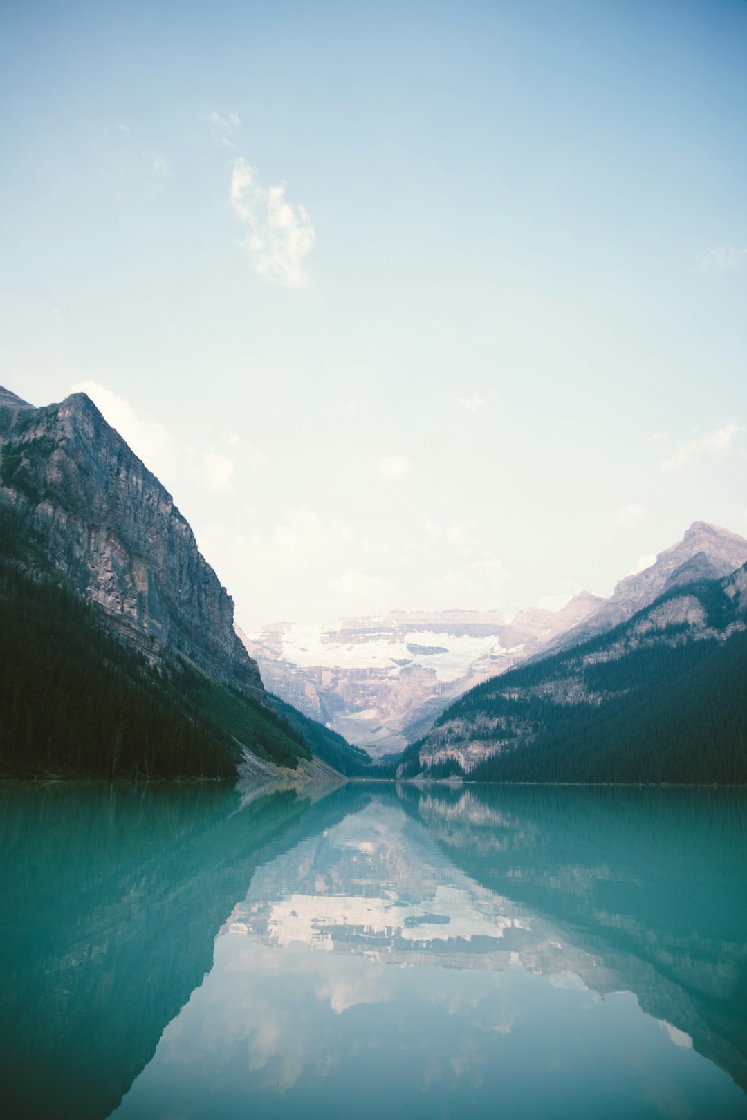 Lake Louise, Canada, landscape photography, soft tones, clear sky, reflection of the mountains in the water, shot on a film camera, wide angle shot, natural light, tranquil mood, blue and green color palette, high resolution, highly detailed. –ar 85:128