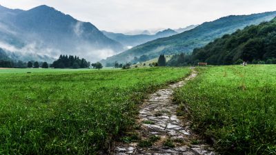 Photo of a stone path leading through green meadows to misty mountains in the background, near Ljub county, in the style of такое photography. Stock photo. --ar 16:9