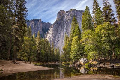 The contest winner, Yosemite National Park, California, during the golden hour, shows a serene river flowing through the valley with towering rock formations in the background, surrounded by lush green trees and clear blue skies, with a sense of tranquility and natural beauty. Photography, the shot used a Canon EOS5D Mark IV camera with a wide-angle lens to capture the panoramic view, in the style of nature photography. --ar 128:85