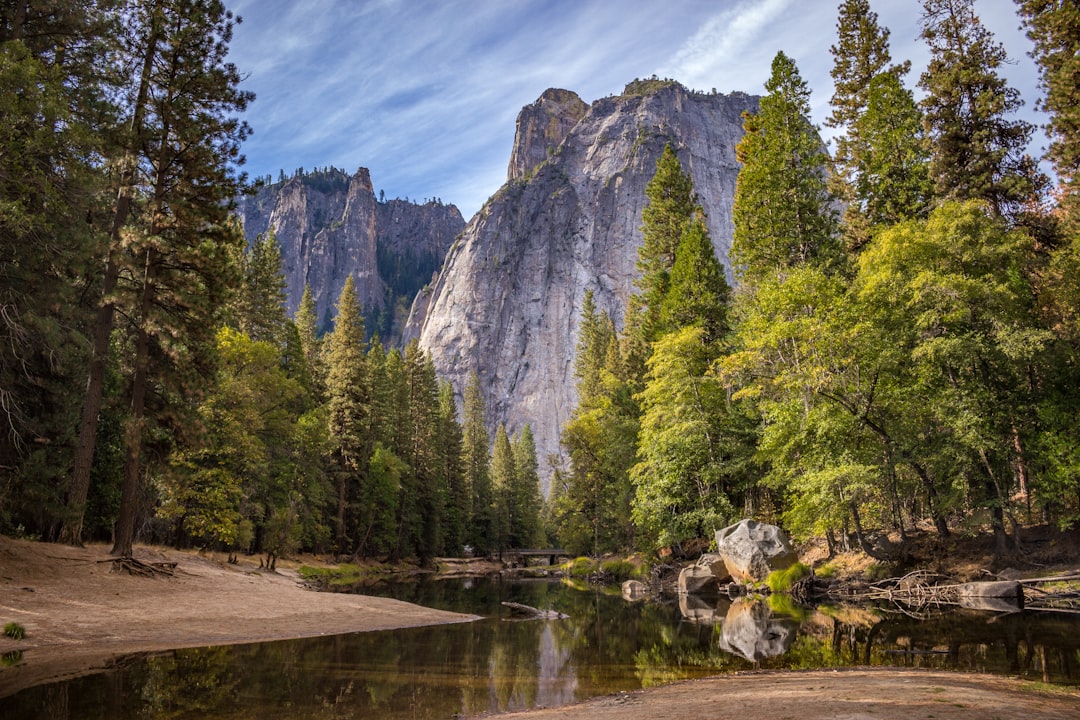 The contest winner, Yosemite National Park, California, during the golden hour, shows a serene river flowing through the valley with towering rock formations in the background, surrounded by lush green trees and clear blue skies, with a sense of tranquility and natural beauty. Photography, the shot used a Canon EOS5D Mark IV camera with a wide-angle lens to capture the panoramic view, in the style of nature photography. –ar 128:85