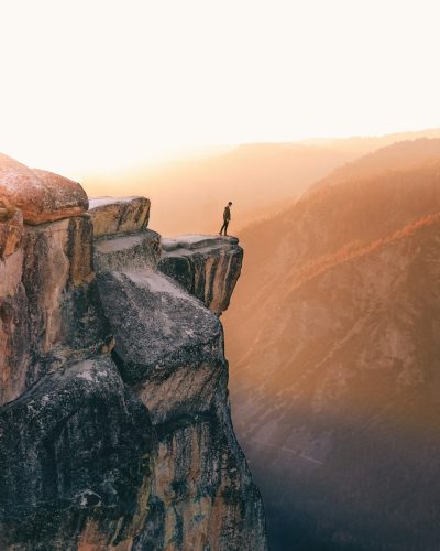 A person standing on the edge of an iconic rock formation, overlooking vast landscapes below, symbolizing solitude and connection with nature, bathed in soft golden light, focus on face, sunrise, morning in Yosemite National Park, photo in the style of [Carsten Meyerdierks](https://goo.gl/search?artist%20Carsten%20Meyerdierks). --ar 51:64