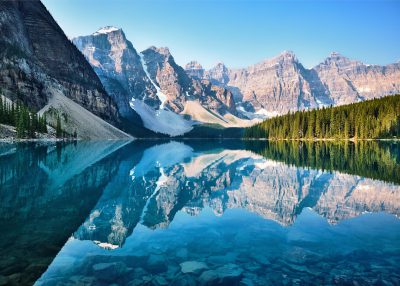 A stunning photograph of the picturesque Moraine Lake in Canada, reflecting crystal clear waters and majestic mountains. The scene captures the serene beauty of nature with towering peaks standing tall against a blue sky backdrop. The photograph was taken in the style of [Ansel Adams](https://goo.gl/search?artist%20Ansel%20Adams), known for his black-and-white landscape photographs of American national parks and wilderness areas. --ar 128:91