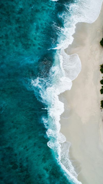 Beautiful aerial view of the beach, waves crashing on white sand and turquoise water. National Geographic photography style drone shot from a top down perspective in a minimalist, high resolution, high definition style with sharp focus and sharp details for a super realistic, hyperrealistic and very detailed look with high quality. --ar 71:128