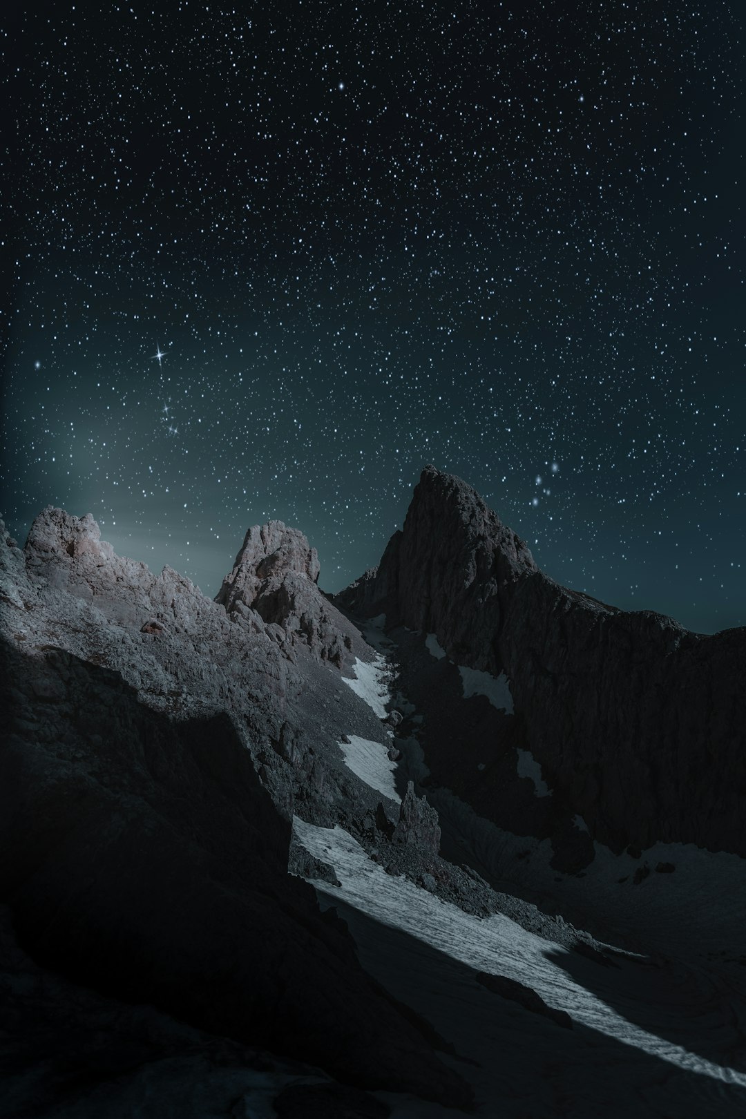 Realistic photography of mountain peaks at night, stars in the sky, dark and mysterious atmosphere, high contrast between light from behind and darkness below, sharp details on snow-covered rocks, moonlight casting long shadows over the scene, creating an ethereal feeling of wonder. –ar 85:128