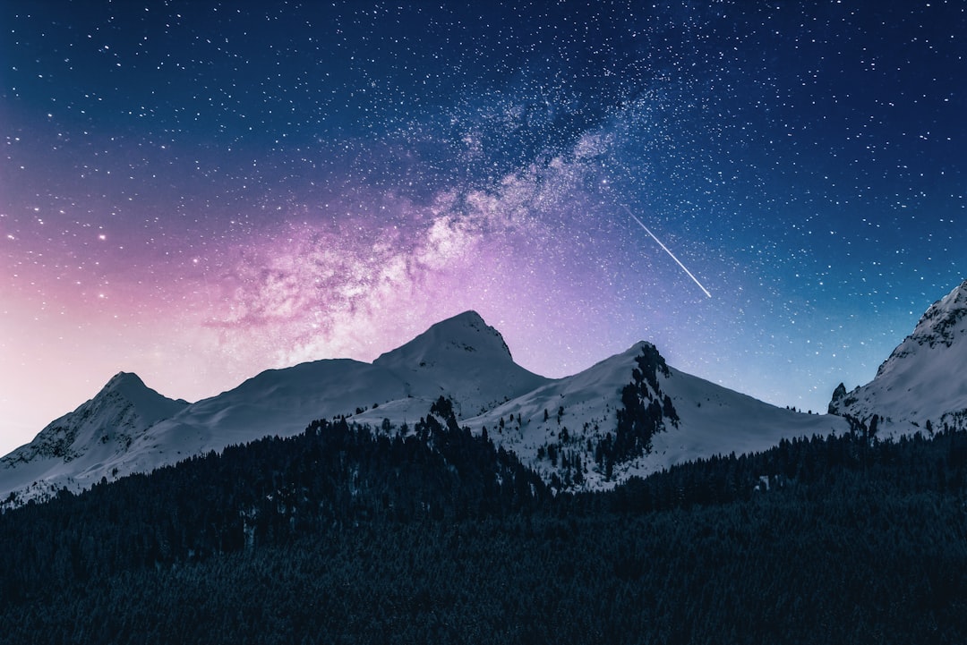 Beautiful night sky with stars and a shooting star over snowy mountains, with a purple pink and blue color gradient, a forest landscape, in the style of high resolution photography. –ar 128:85